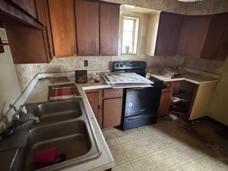 Kitchen before: dark cabinets, peeling wallpaper and a worn floor