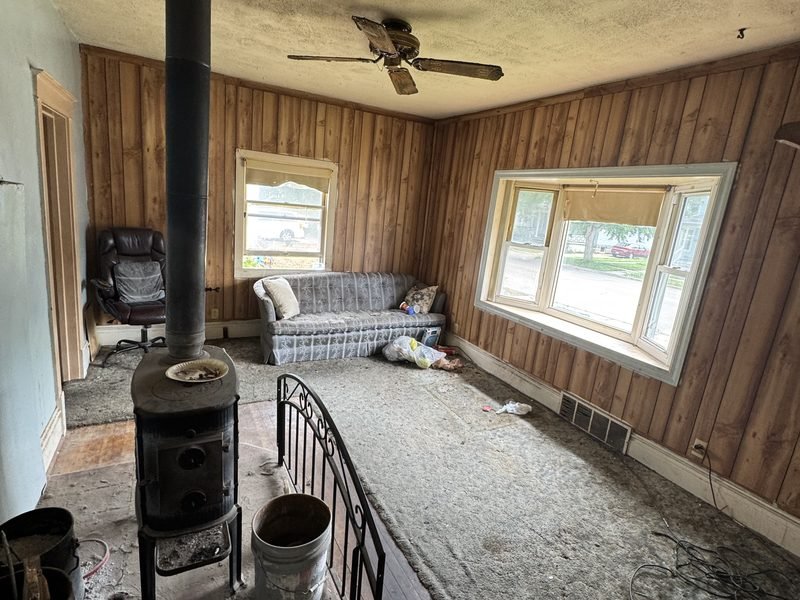 Living room as found: wood paneling, a wood stove and stained carpet