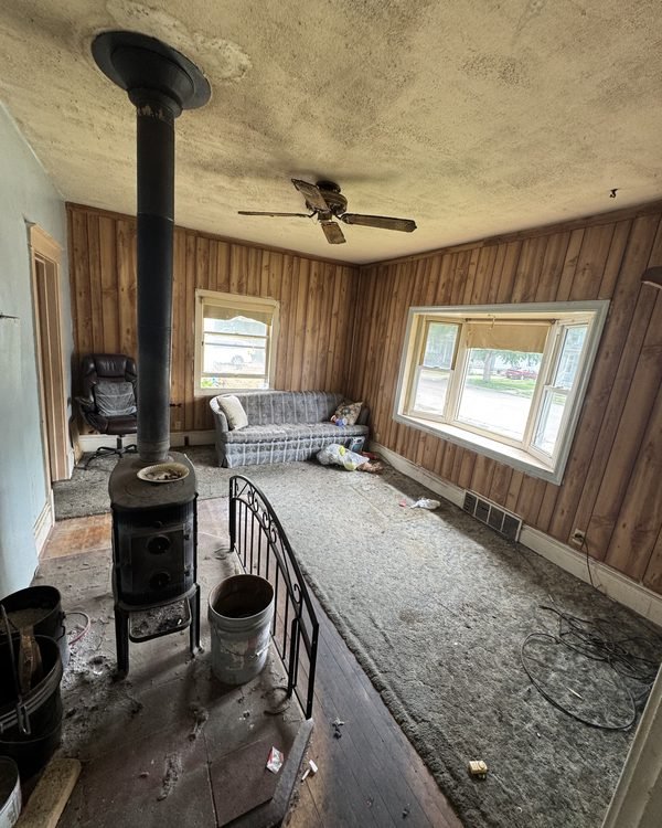 Living room with wood paneling, a wood stove and stained carpet, as found