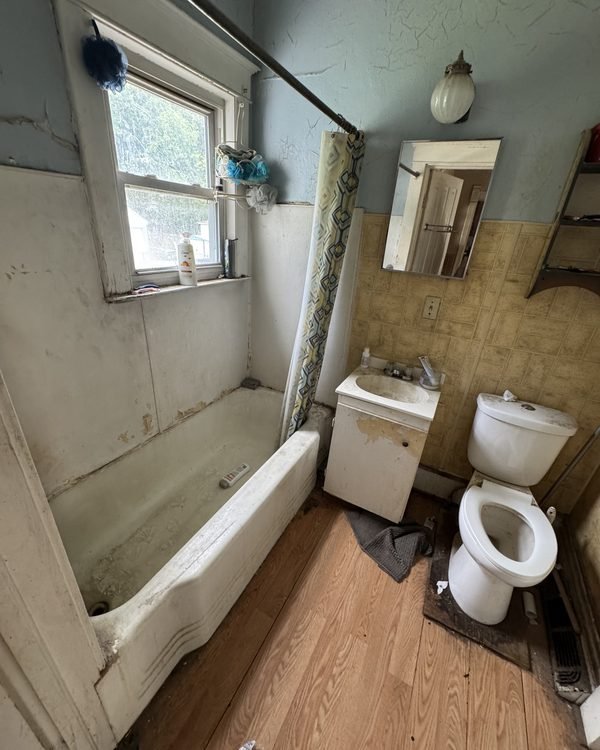 Old bathroom with a stained tub, peeling paint and worn fixtures, as found