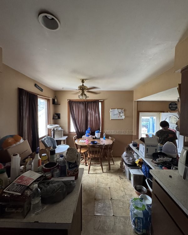 Cluttered kitchen and dining room with belongings on every surface, as found