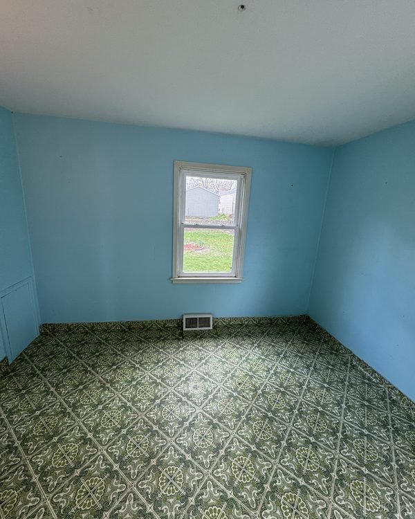Empty blue bedroom with patterned green vinyl floor tile, as found